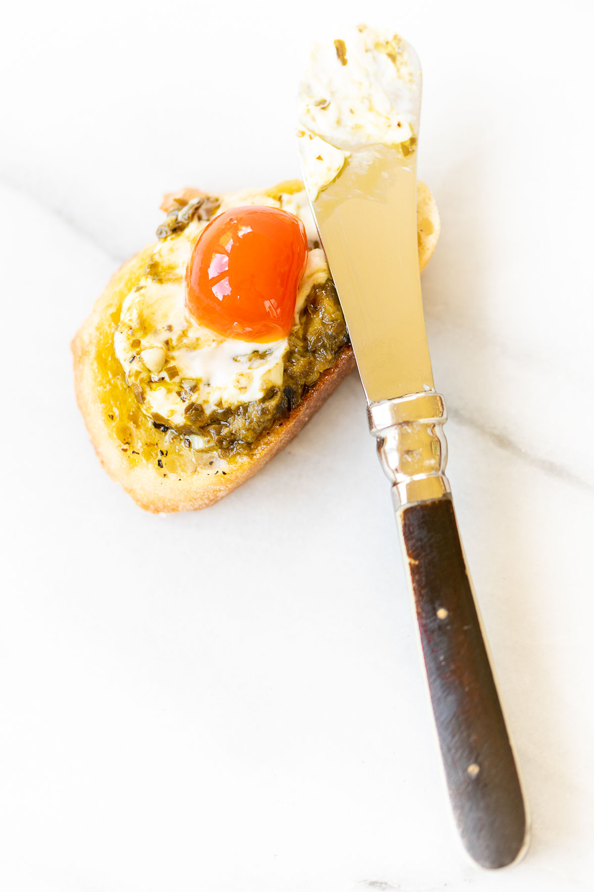 A piece of bread with an egg on it and a pesto cheese dip.