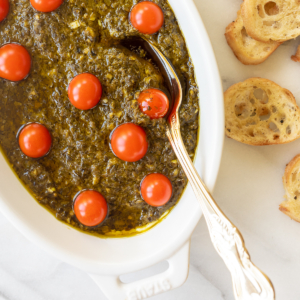 A white dish with pesto and cherry tomatoes, perfect as a refreshing and easy appetizer dip.