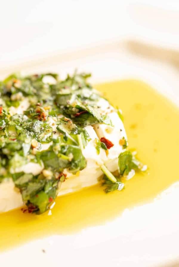 White platter with a cream cheese appetizer, marinated cheese recipe in herbs and oil.
