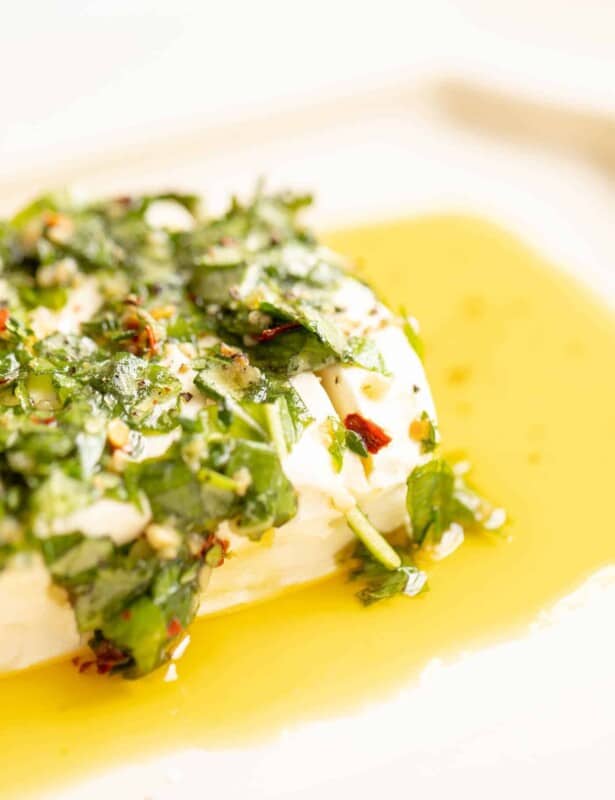 White platter with a cream cheese appetizer, marinated cheese recipe in herbs and oil.