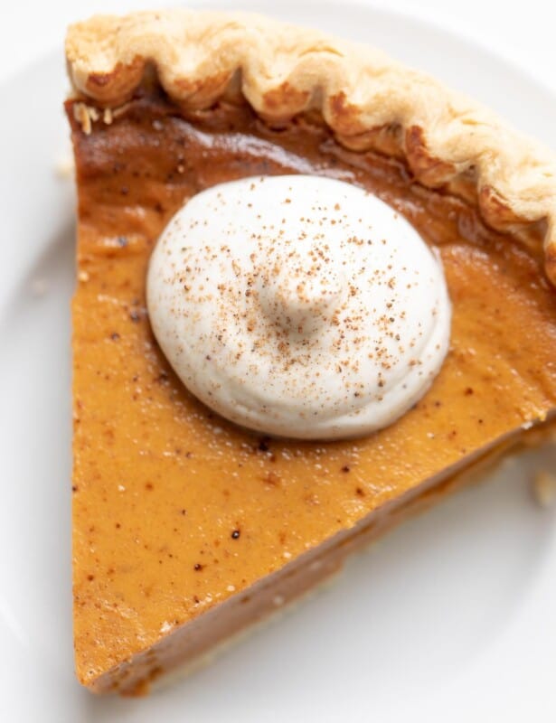 Pumpkin pie topped with egg nog whipped cream on a white plate.