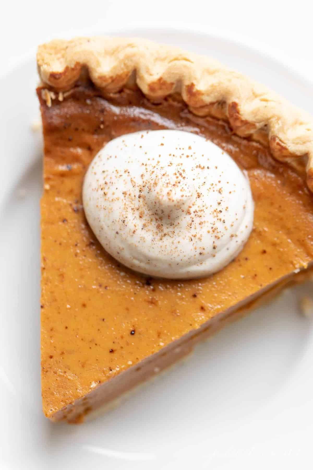 Pumpkin pie topped with egg nog whipped cream on a white plate. 
