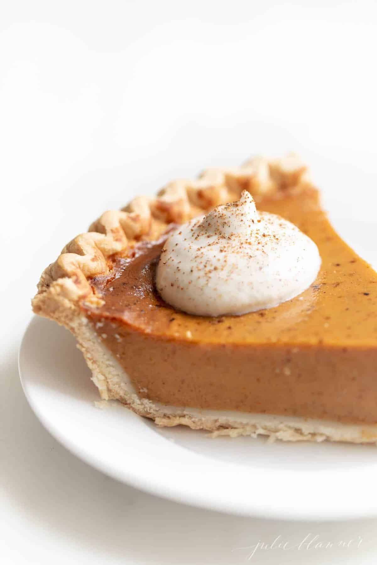 Pumpkin pie topped with eggnog whip cream on a white plate. 