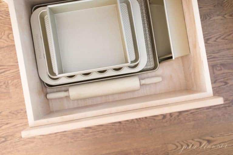 A kitchen cabinet drawer filled with baking sheets and a rolling pin.