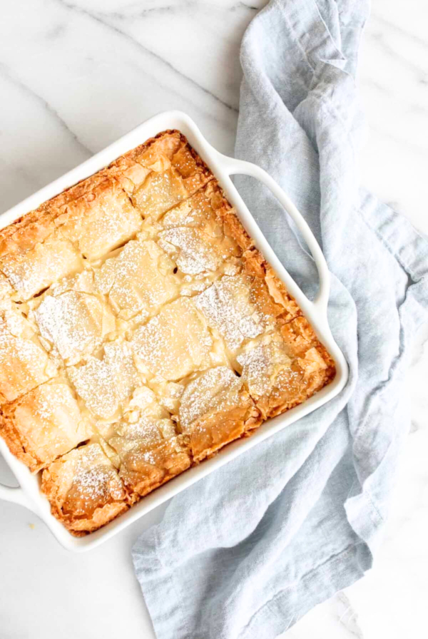 A white baking dish with a square of apple pie and gooey butter cake.