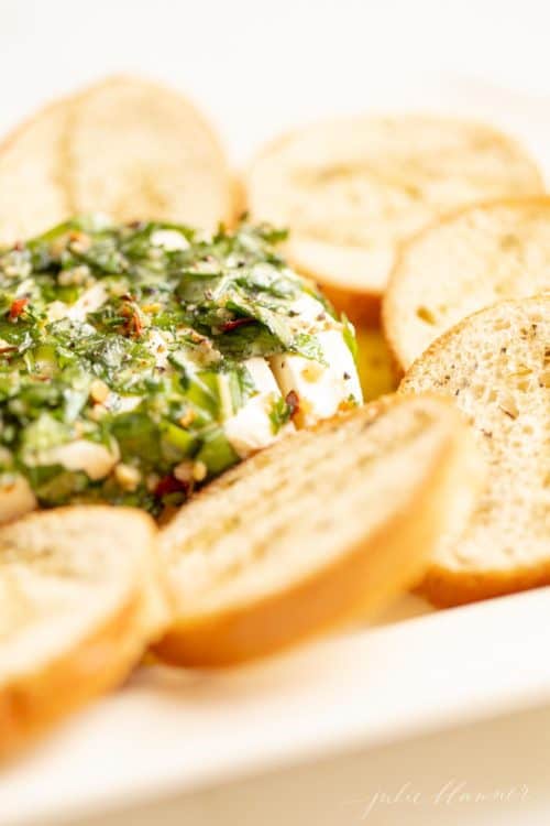 A cream cheese appetizer with marinated cream cheese recipe in herbs and oil, crostini to the side.