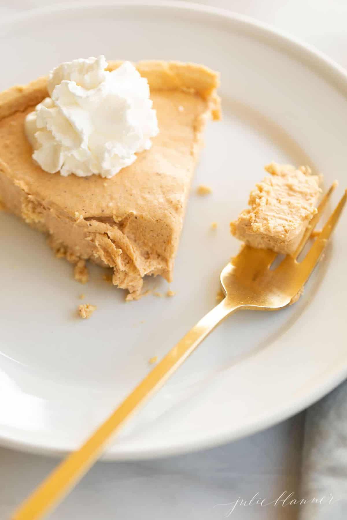 White plate with a slice of pumpkin cheesecake, gold fork to the side.