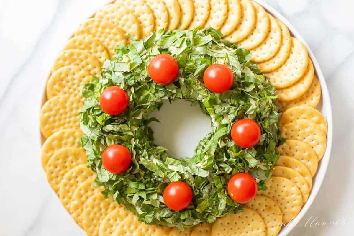 A pesto cheeseball Christmas wreath appetizer surrounded by crackers on a platter.