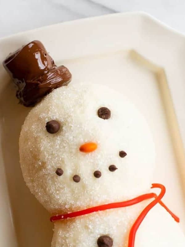 White surface, snowman cheeseball on a platter, chocolate chip smile.