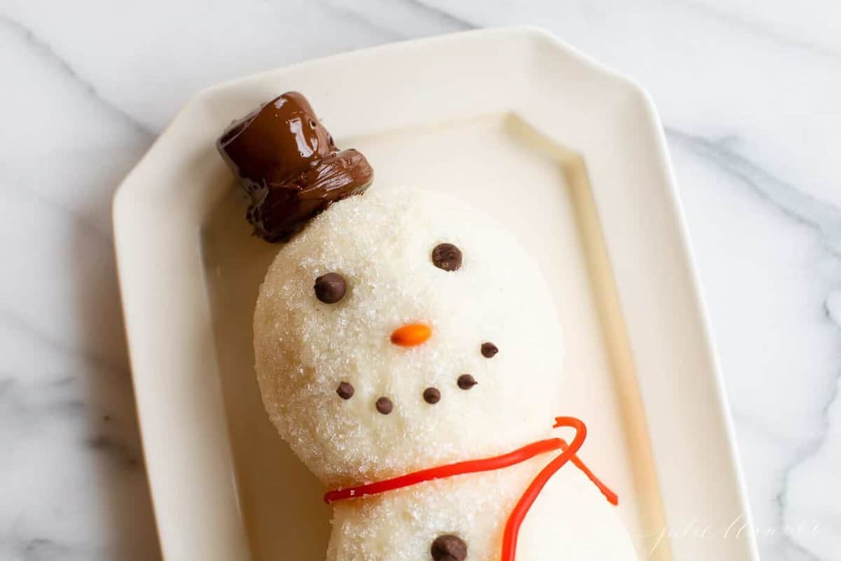 White surface, snowman cheeseball on a platter, chocolate chip smile.