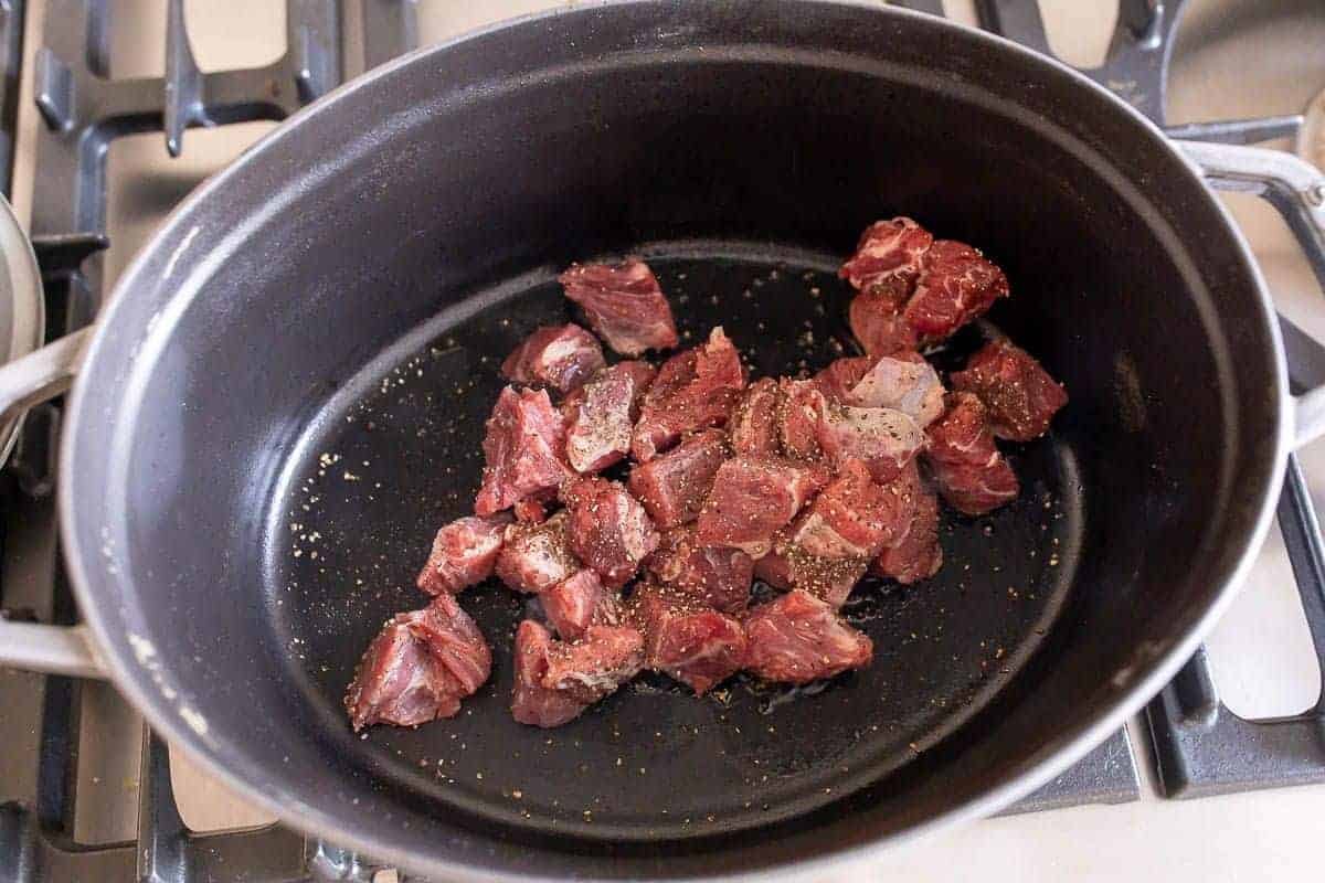 A large oval cast iron pot with chunks of beef inside.