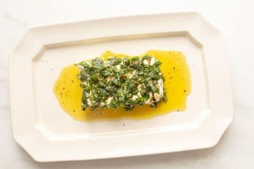 A marinated herb cream cheese block on a white platter.