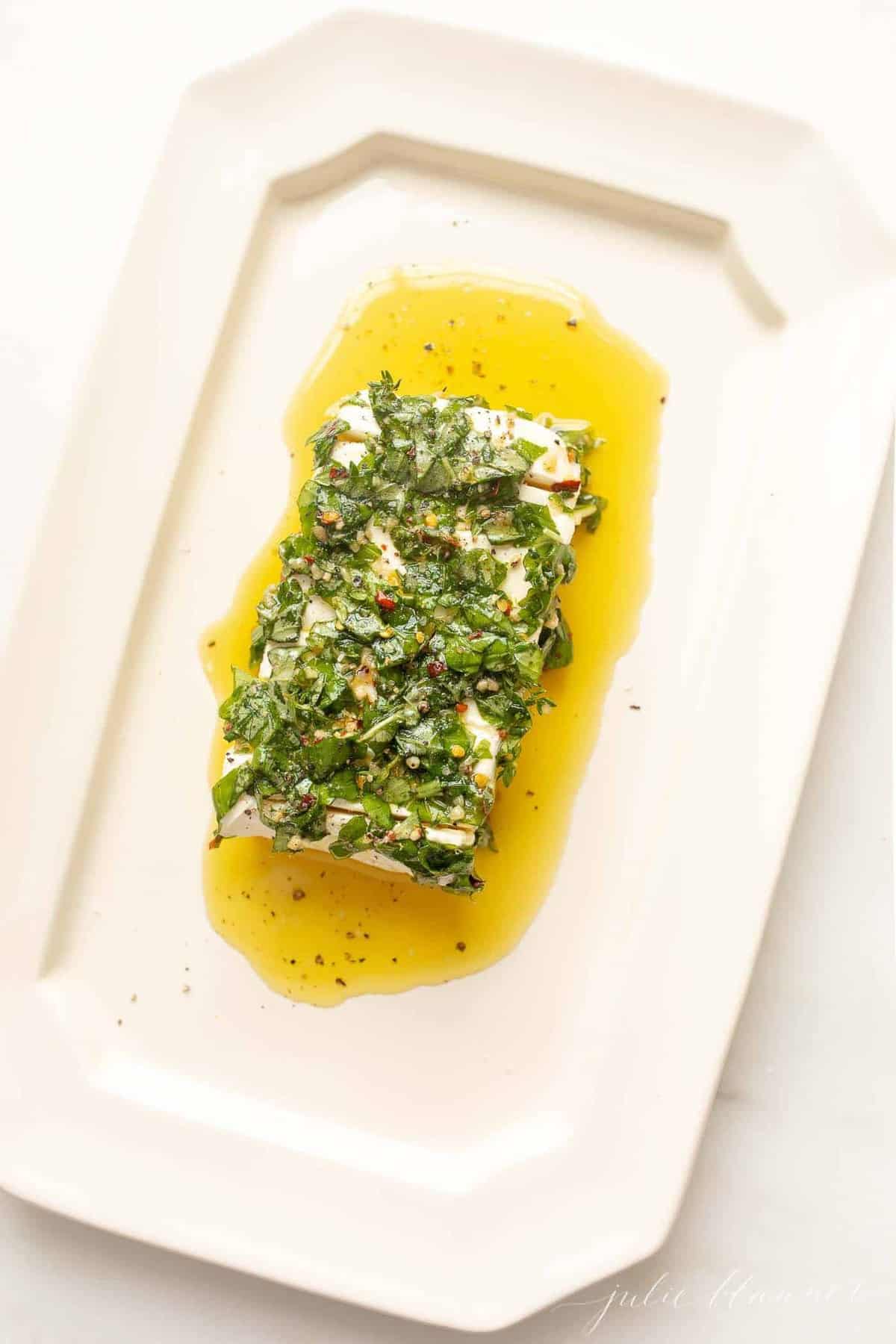 White platter with a cream cheese appetizer, marinated in herbs and oil.