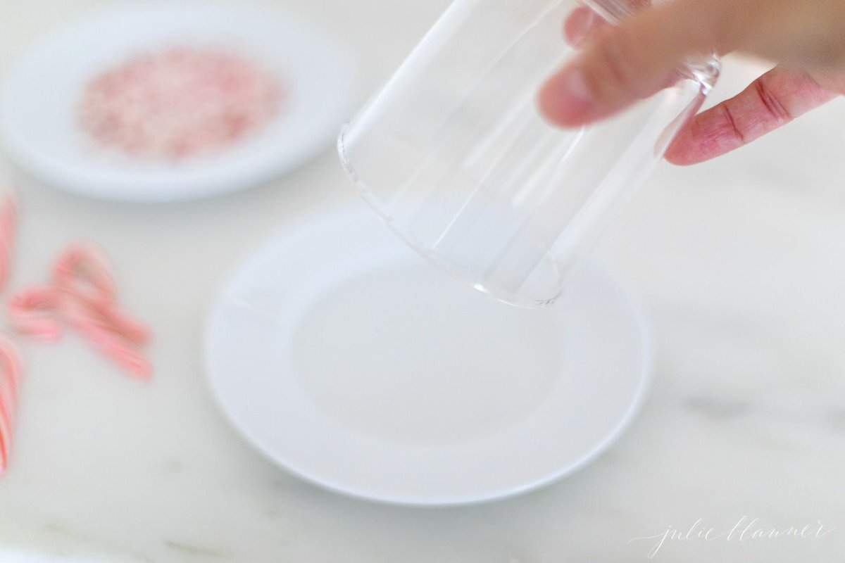 A clear glass being placed upside down onto a plate of crushed peppermint.