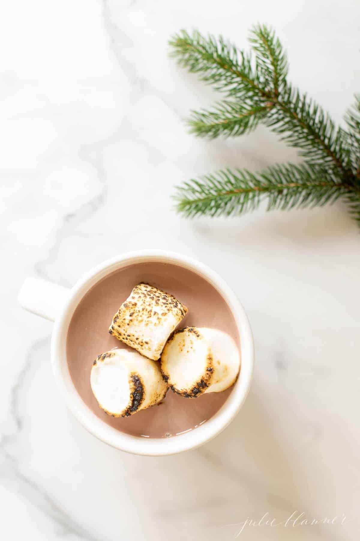 Looking into a mug of peppermint hot chocolate, marshmallows on top, greenery touch to the side.