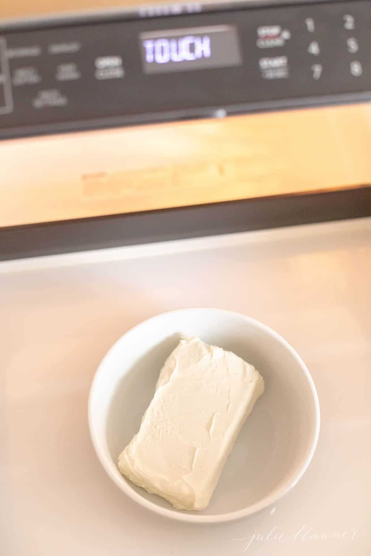 Countertop with a white bowl, block of cream cheese inside.