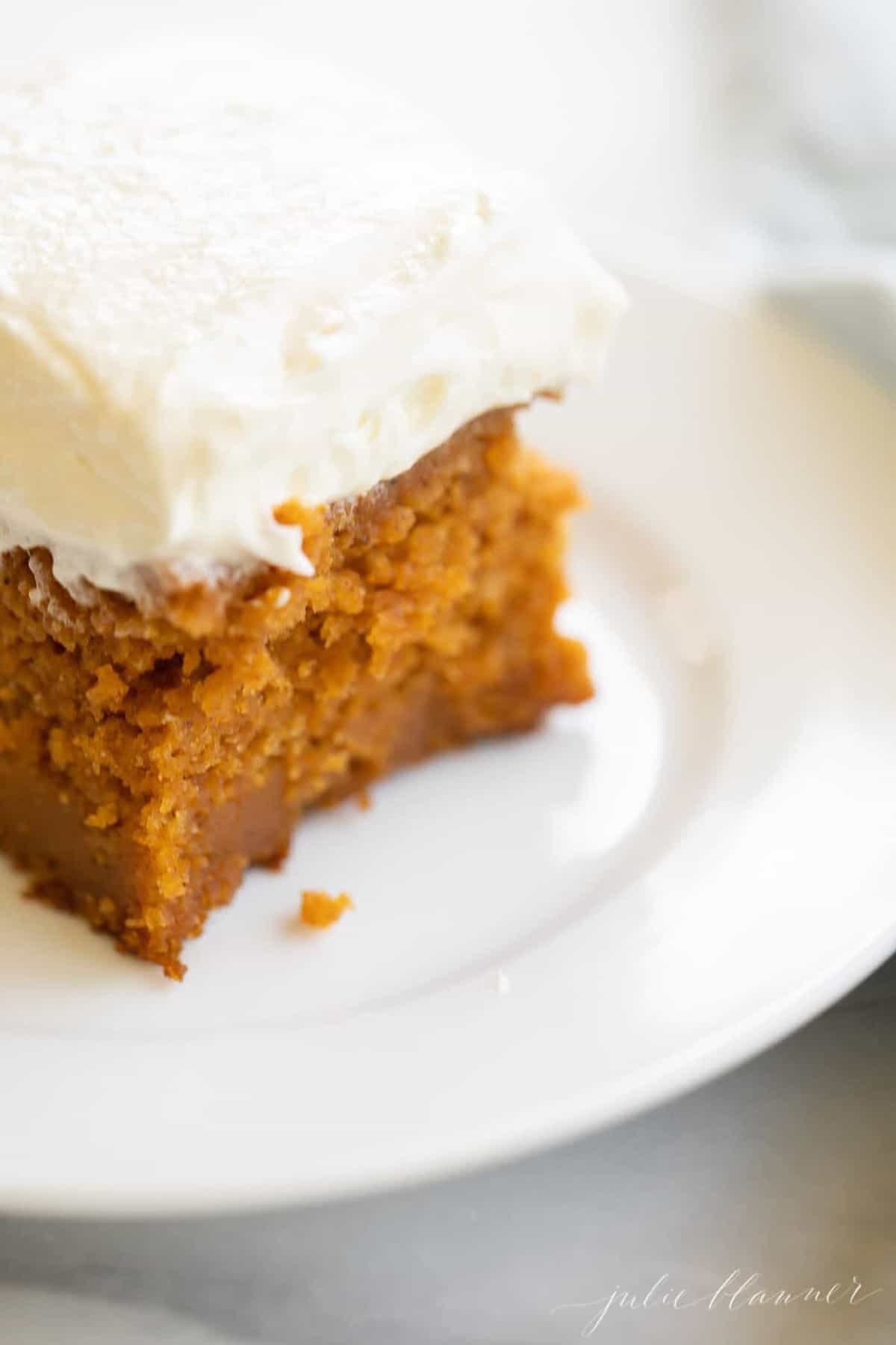 White plate with a slice of pumpkin cake covered in frosting.