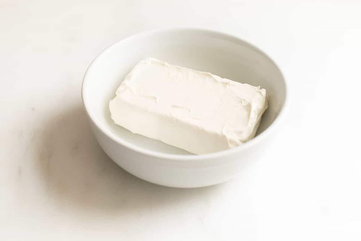 White bowl with a block of cream cheese inside.