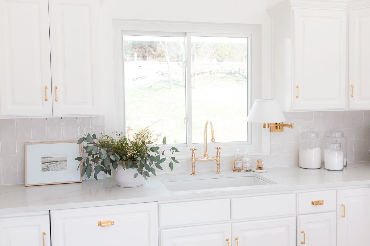 A white kitchen with a brass faucet and a variety of kitchen accessories