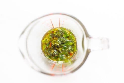 Inside a measuring cup with herbs, garlic and oil.