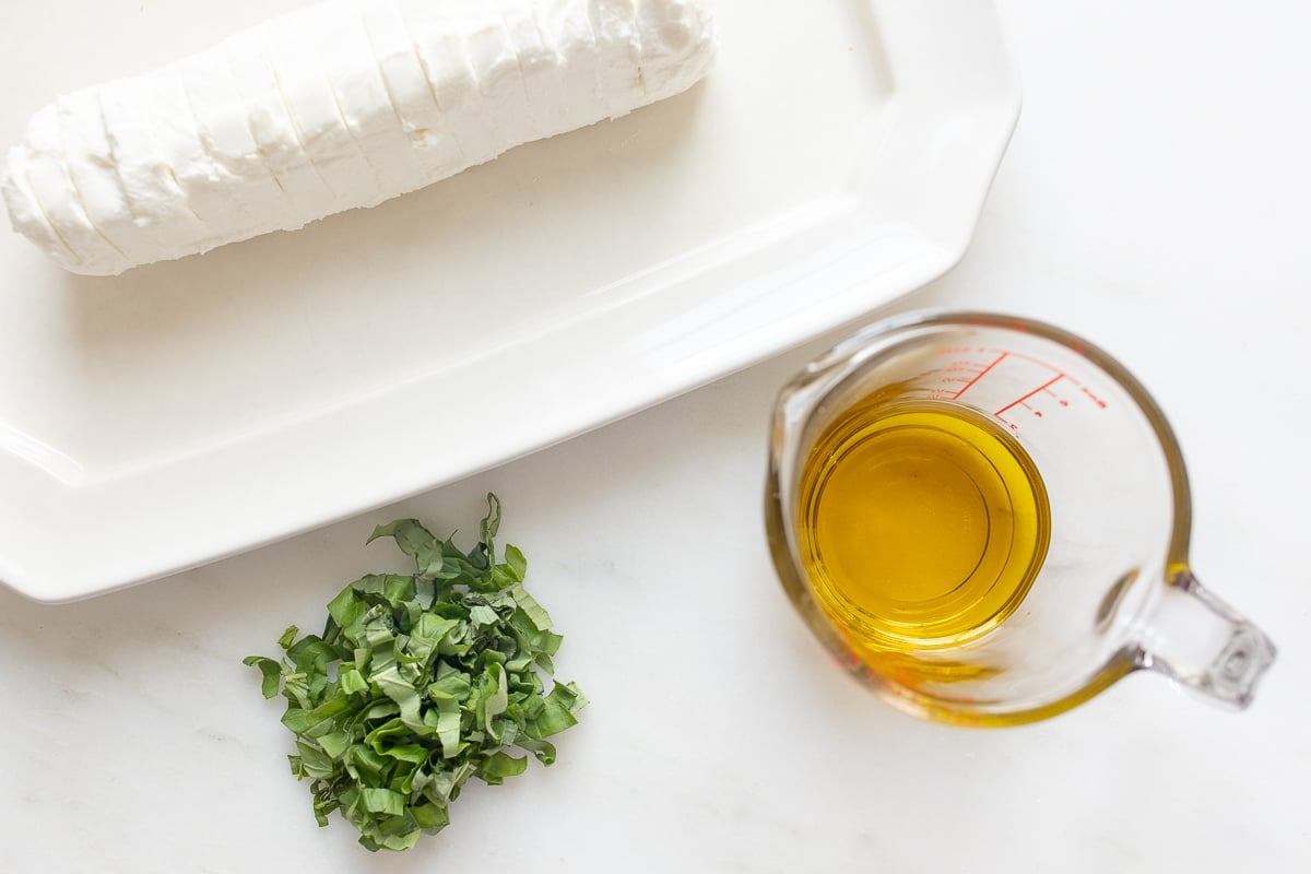 A white plate with chevre goat cheese, herbs, and a measuring cup.