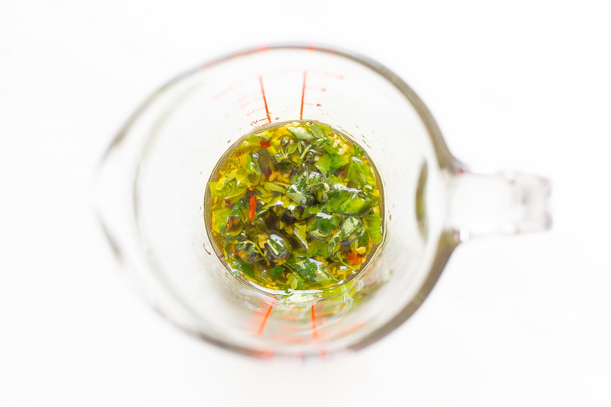 A measuring cup filled with a mixture of greens and herbs enhanced by chevre goat cheese.