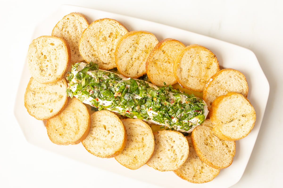 A white plate with a log of marinated goat cheese surrounded by crostini.