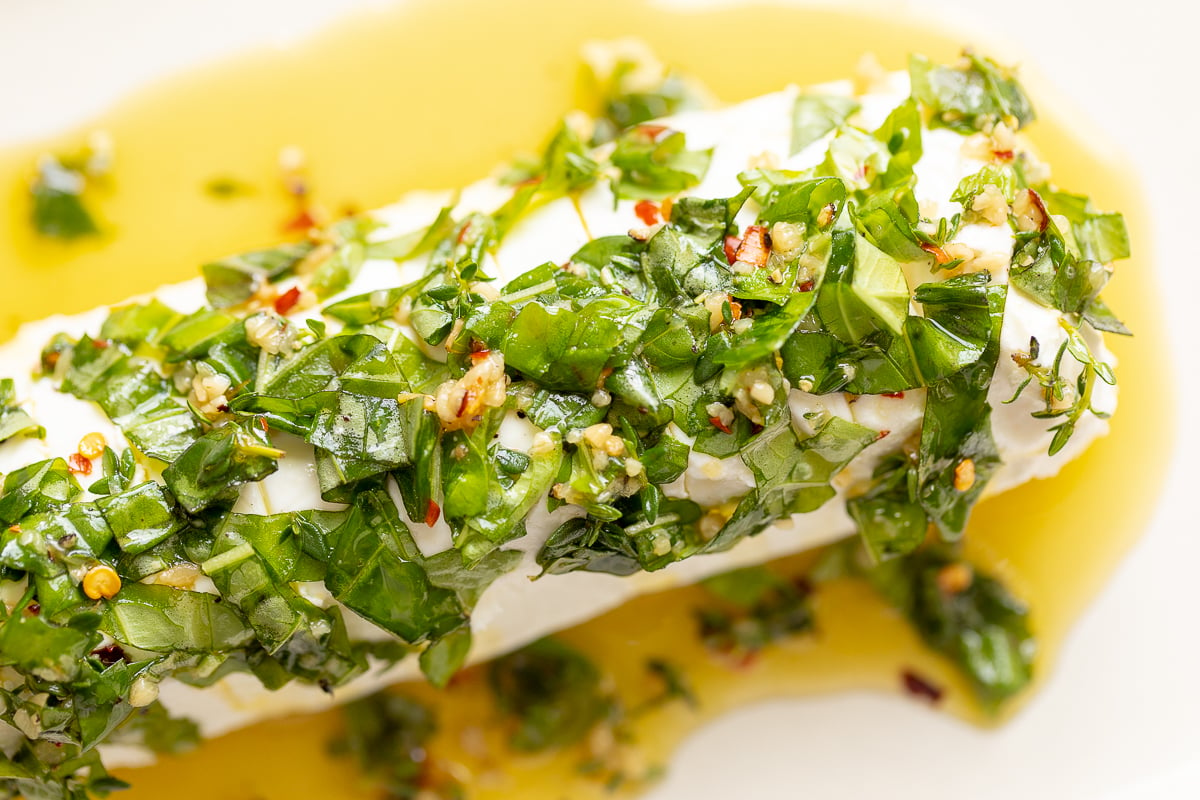 A plate with a piece of fish covered in herbs and topped with goat cheese.