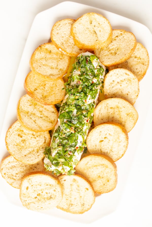 A white plate with a marinated goat cheese appetizer surrounded by crostini.