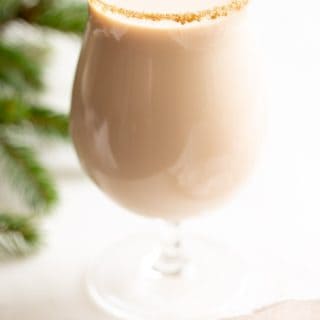A clear glass with an oatmeal cookie cocktail, rimmed in sugar, greenery to the side.