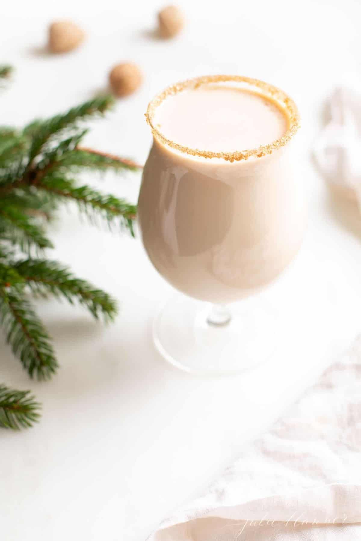 A clear glass with an oatmeal cookie drink, hazelnuts and greenery to the side.