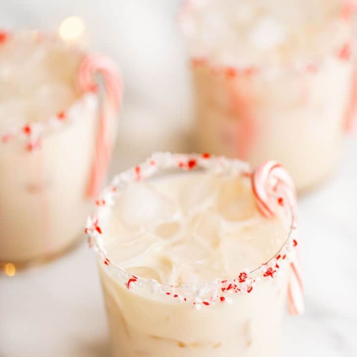 three clear glasses of peppermint cocktails, garnished with a candy cane.