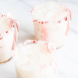 A peppermint white russian cocktail, garnished with a candy cane and crushed peppermint on the rim.