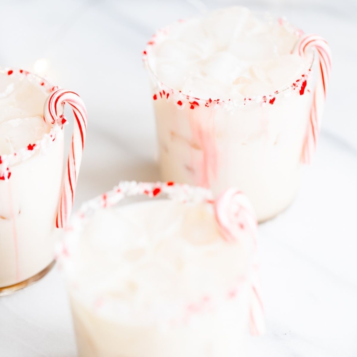 A peppermint white russian cocktail, garnished with a candy cane and crushed peppermint on the rim.