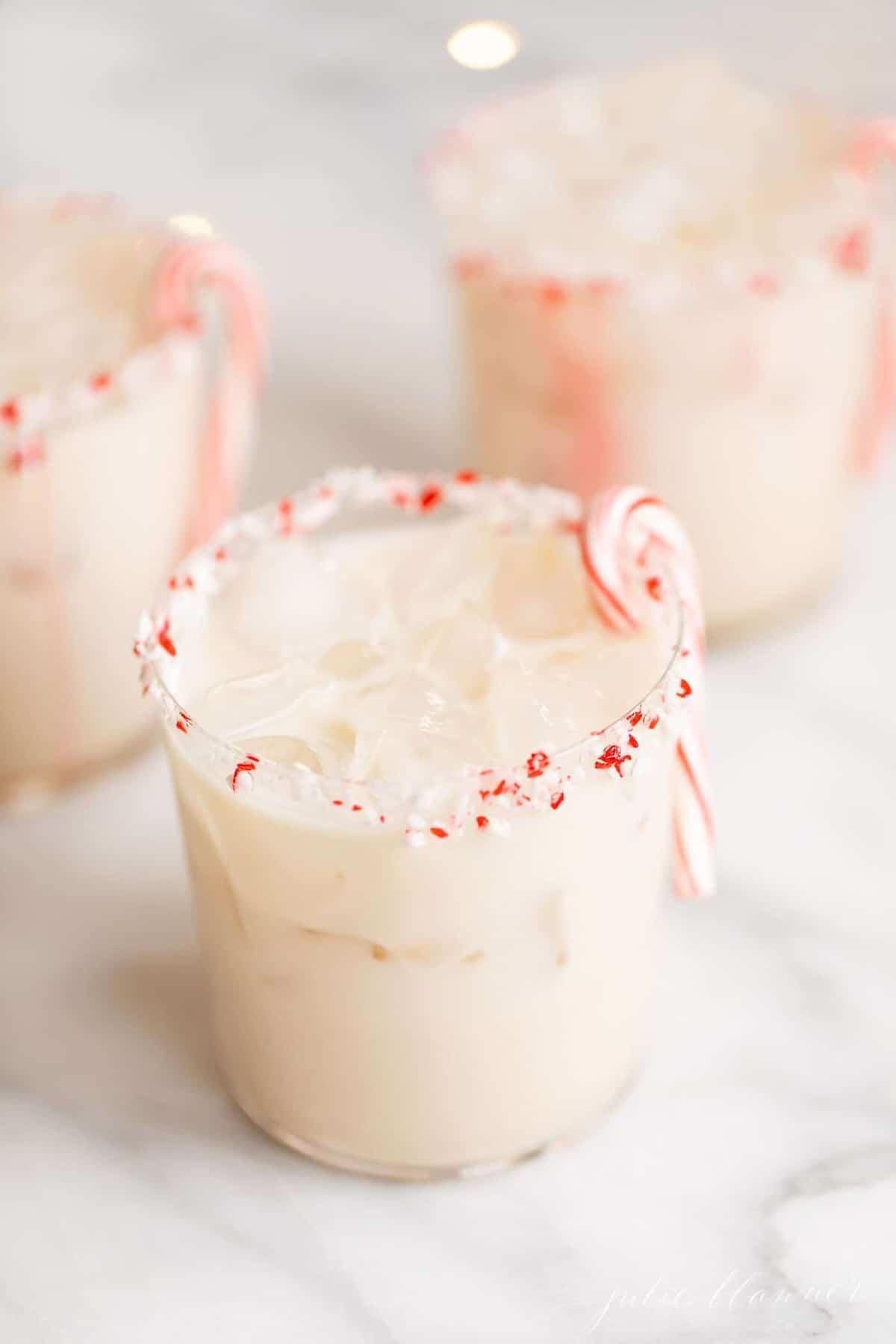 three clear glasses of peppermint cocktails, garnished with a candy cane.