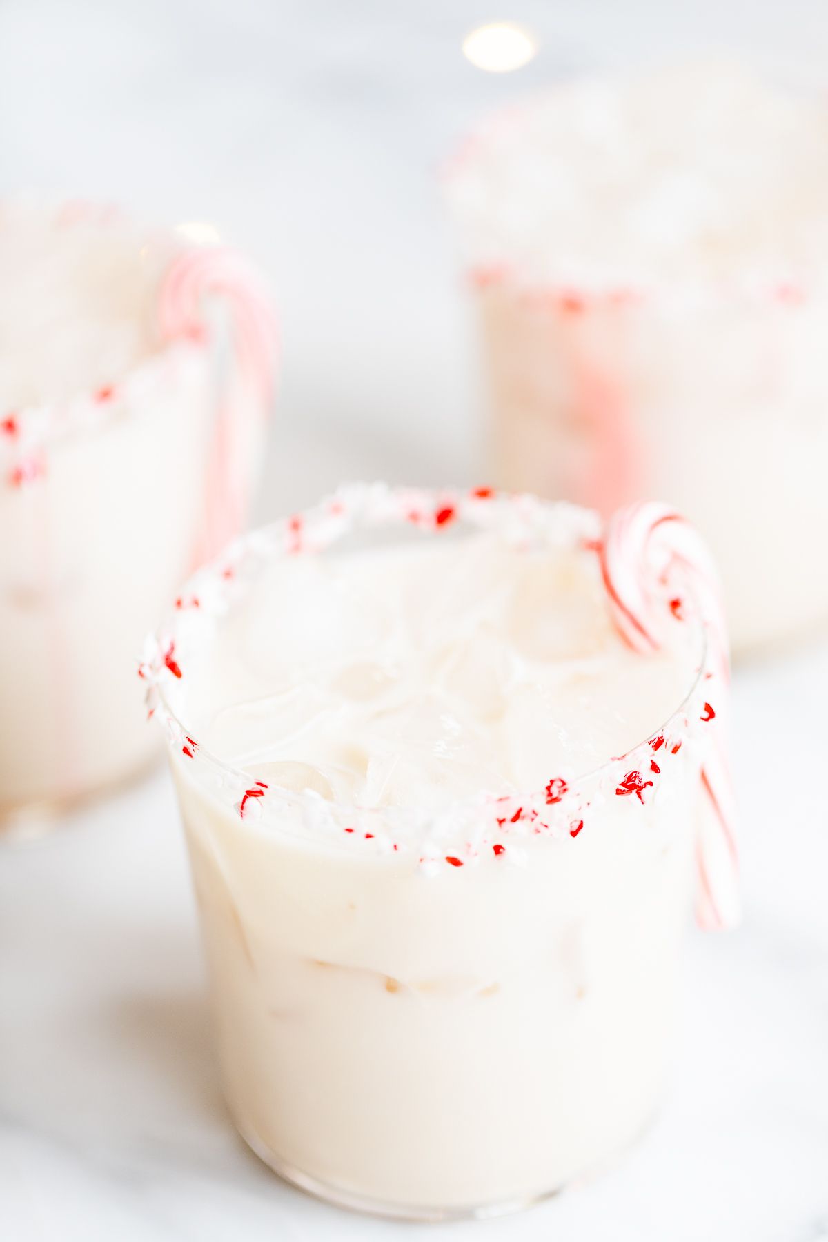 A peppermint white russian cocktail, garnished with a candy cane and crushed peppermint on the rim.