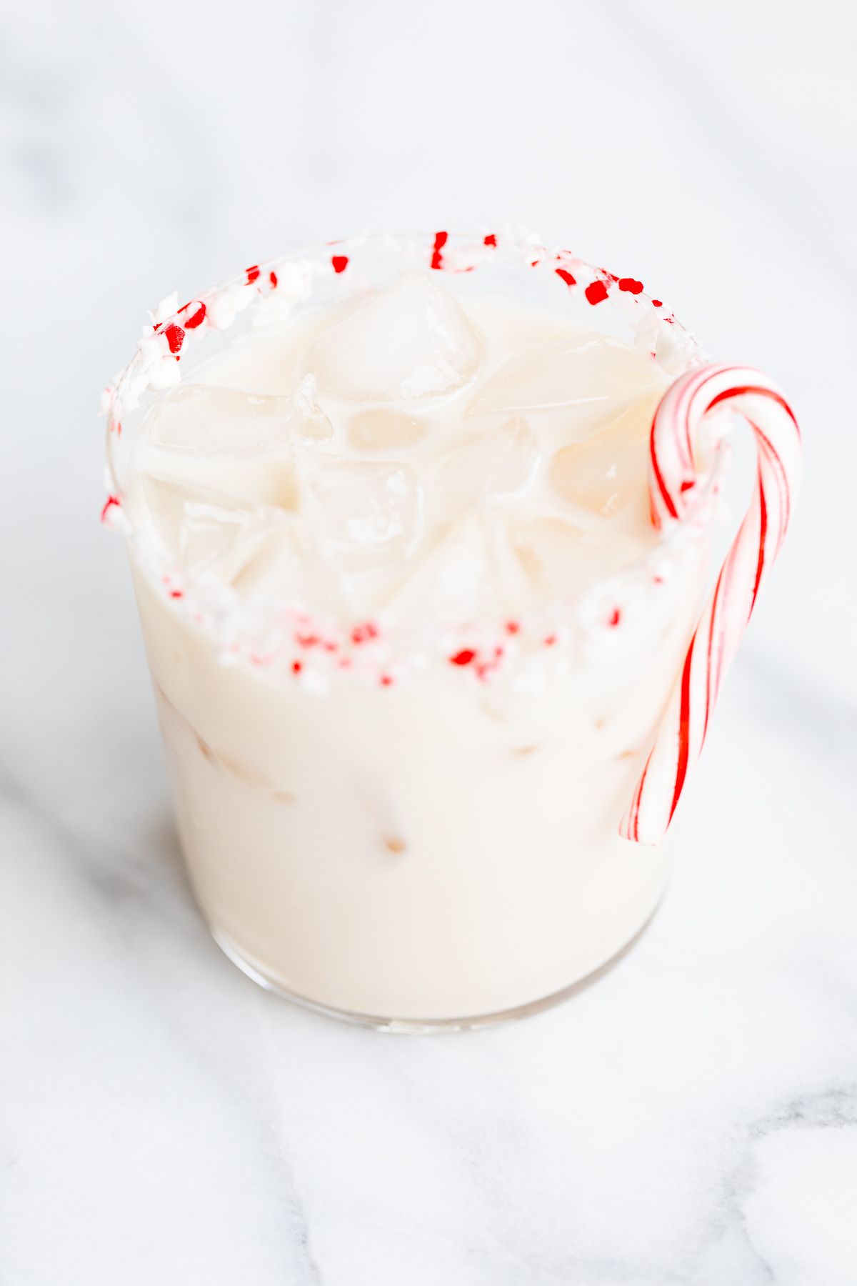 A peppermint white russian cocktail, garnished with a candy cane and crushed peppermint on the rim.