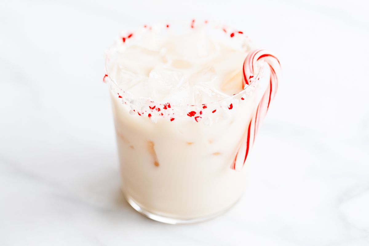 A peppermint white russian cocktail, garnished with a candy cane and crushed peppermint on the rim.
