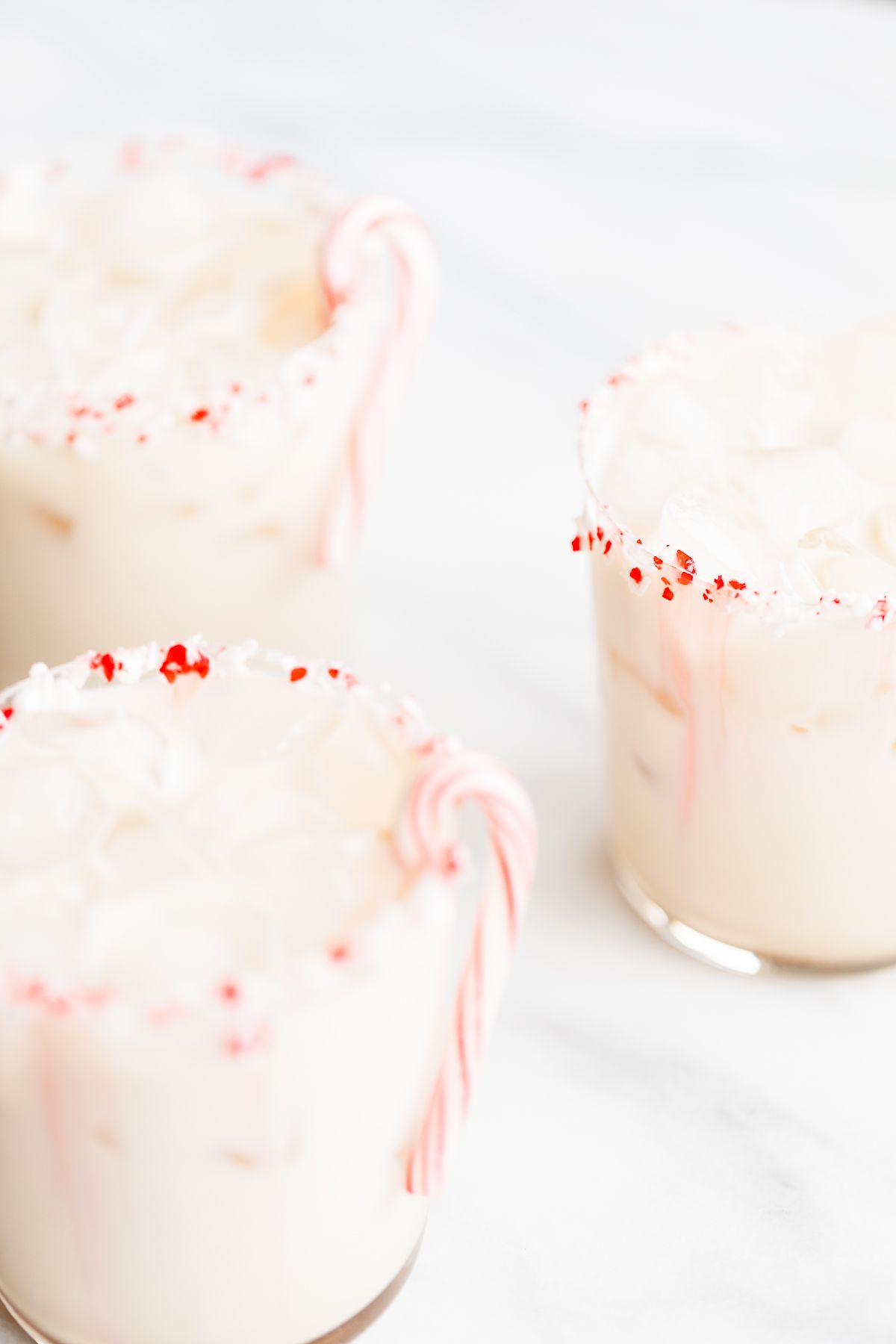 A peppermint white russian cocktail, garnished with a candy cane and crushed peppermint on the rim.