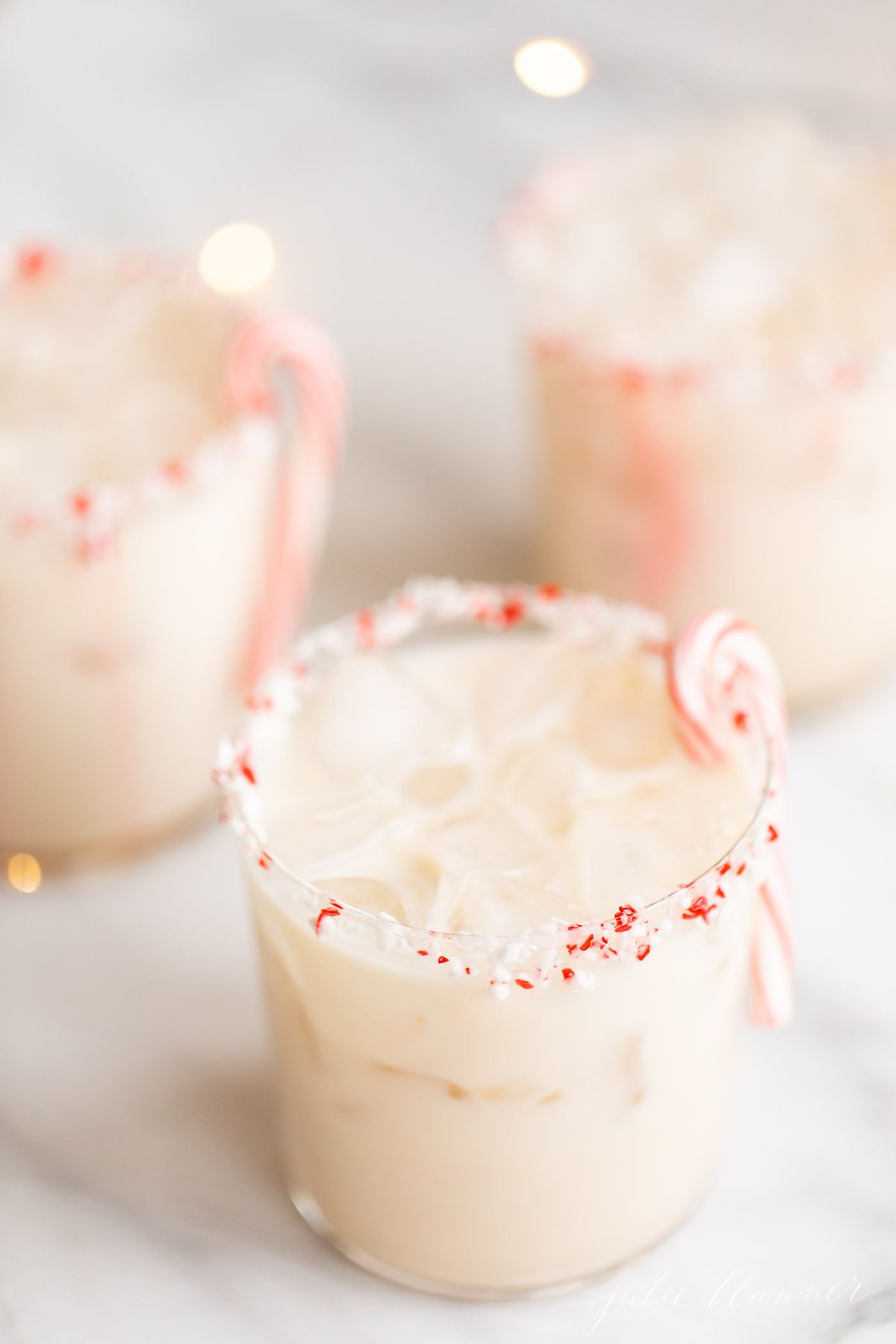 A peppermint white russian cocktail, garnished with a candy cane and crushed peppermint on the rim.