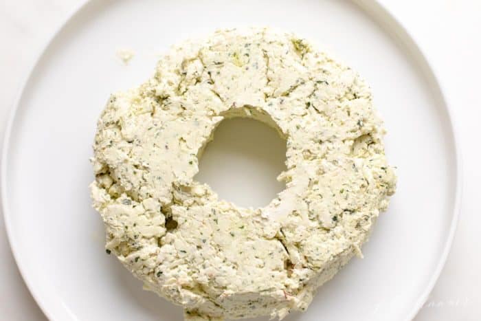 A white surface with a pesto cheeseball wreath appetizer beginning to form.