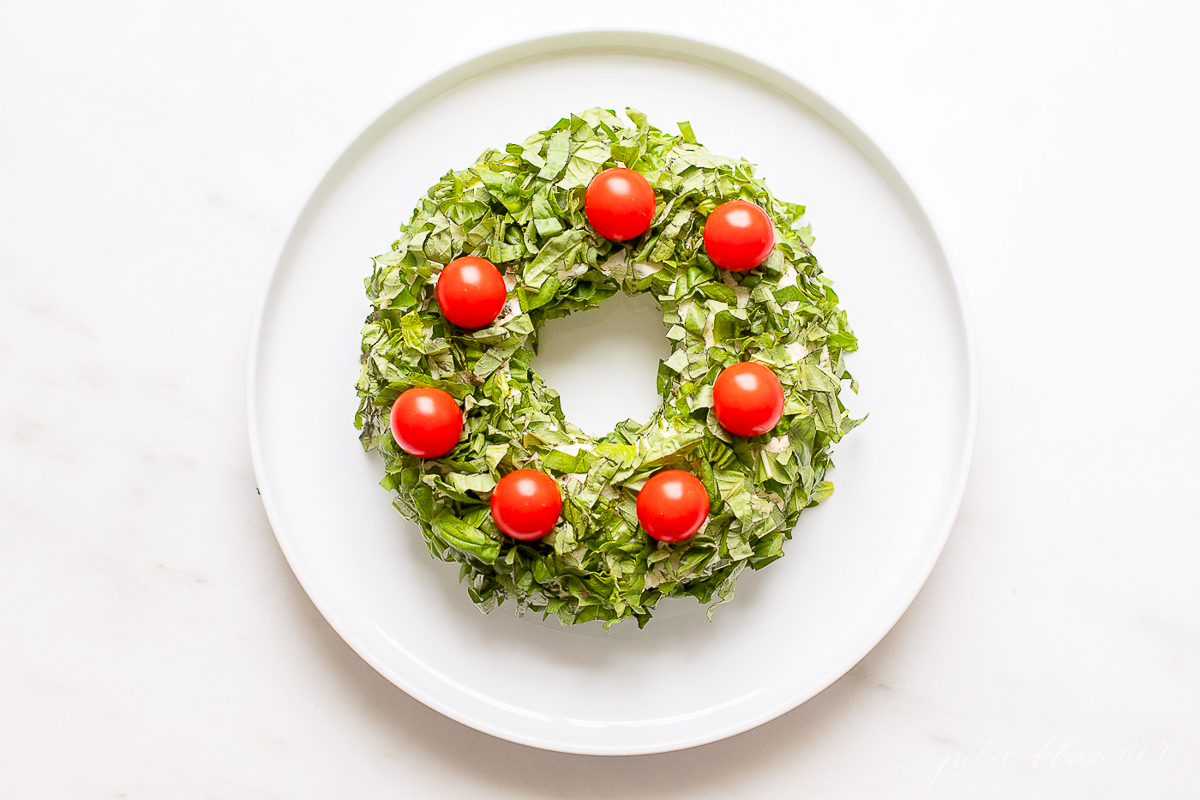 A pesto cheese ball topped with cherry tomatoes on a white plate.
