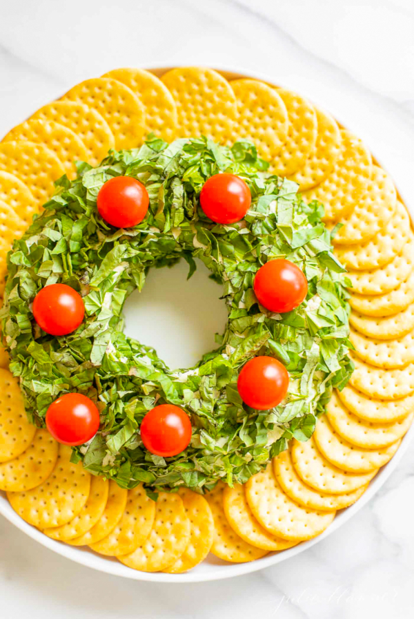 A plate with a wreath made of pesto cheese ball and tomatoes.