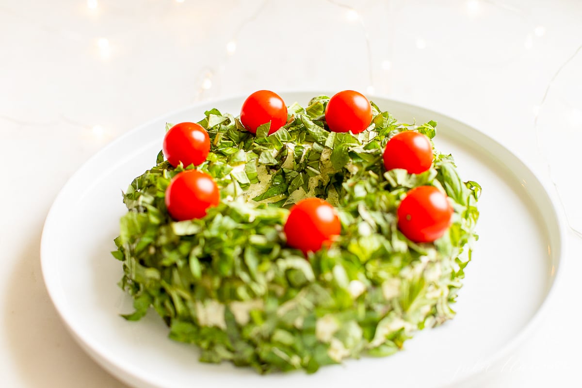 A pesto cheese ball topped with cherry tomatoes on a white plate.