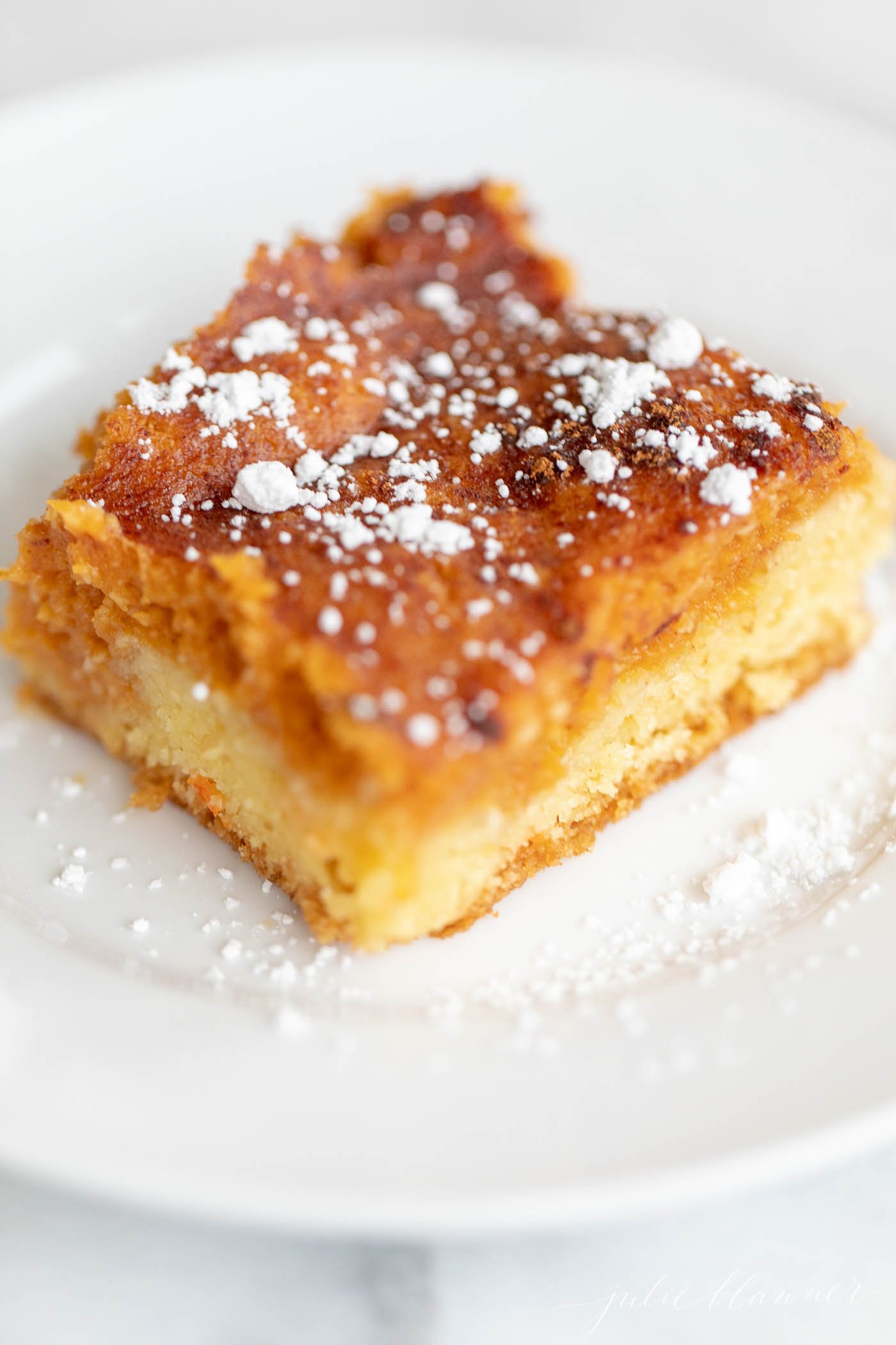 A slice of pumpkin gooey butter cake on a white plate, dusted with powdered sugar.