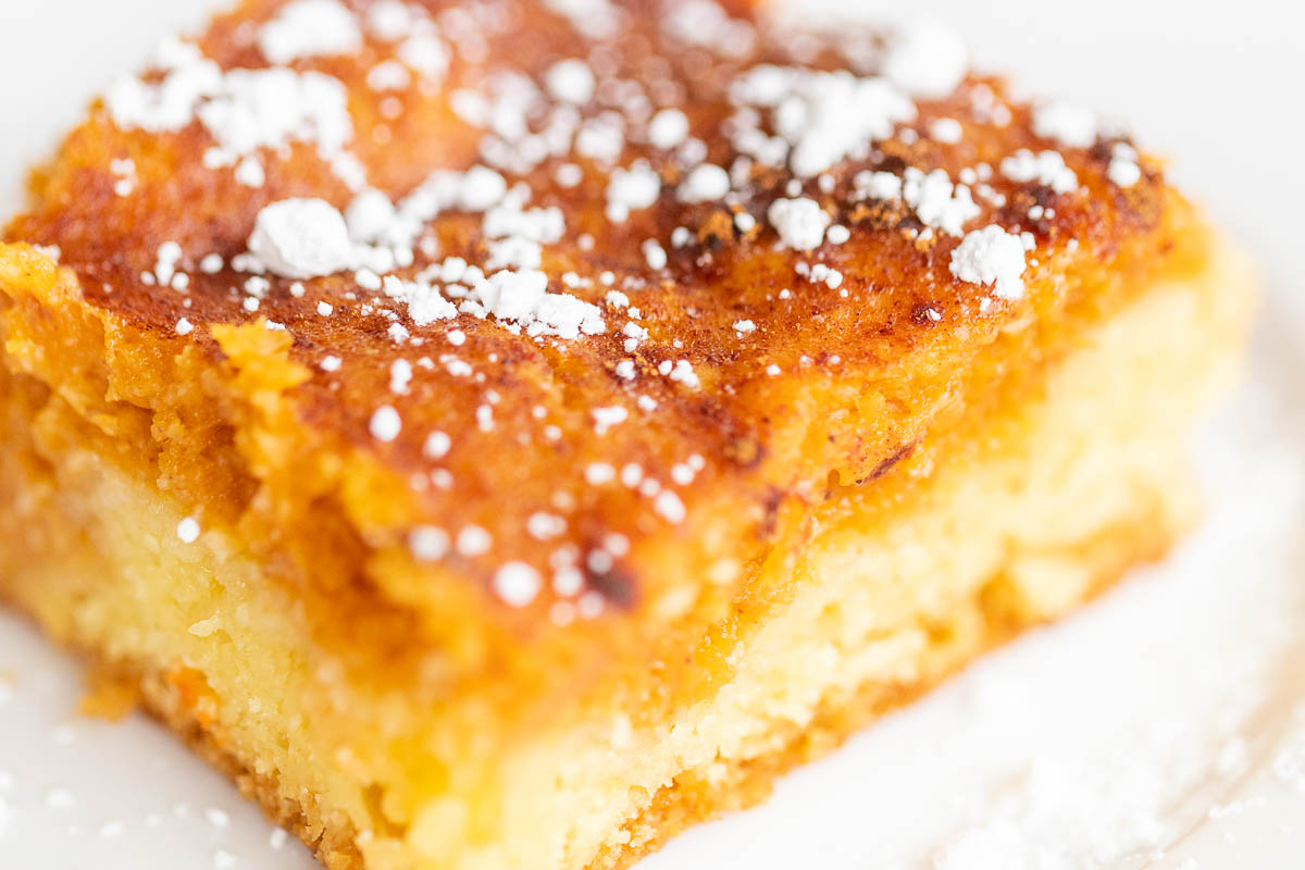 A slice of pumpkin gooey butter cake on a white plate, dusted with powdered sugar.