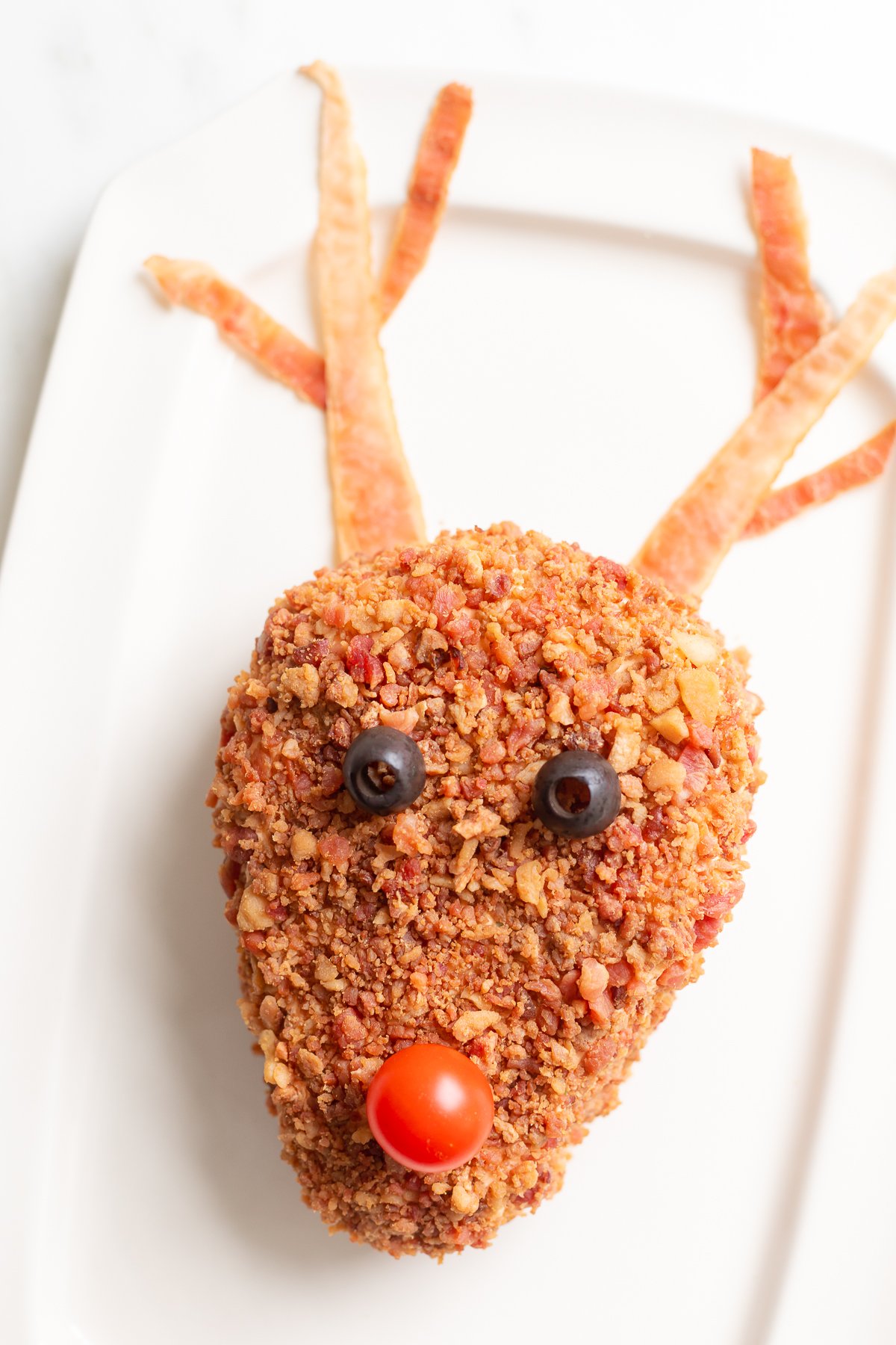 A plate with a bacon covered reindeer cheeseball on it.