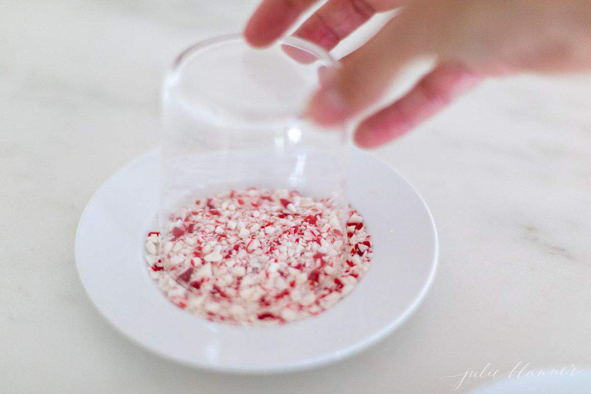 A clear glass, hand reaching to dip it into crushed peppermint for garnish.