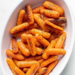 A white cast iron baking pan filled with roasted baby carrots