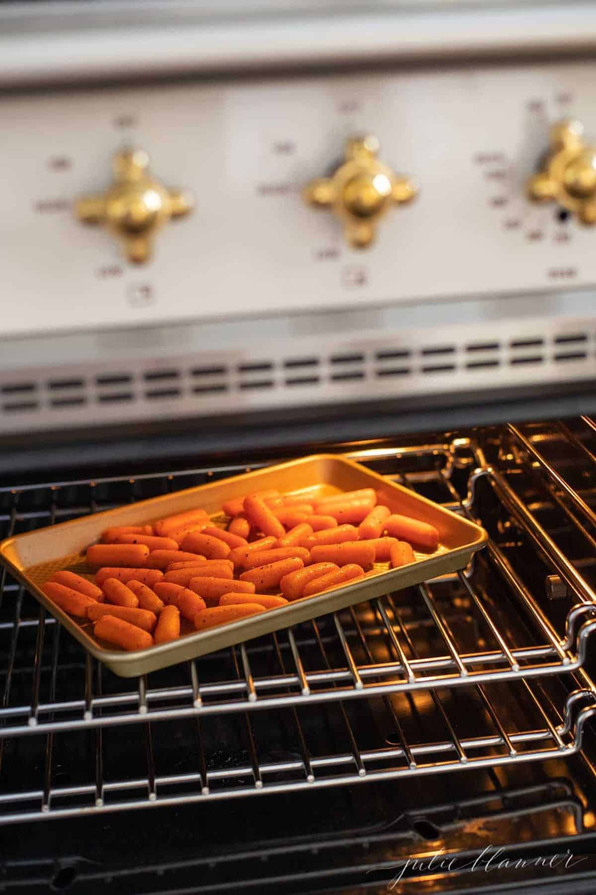 Looking inside a range, with a gold sheet of roasted dill carrots.